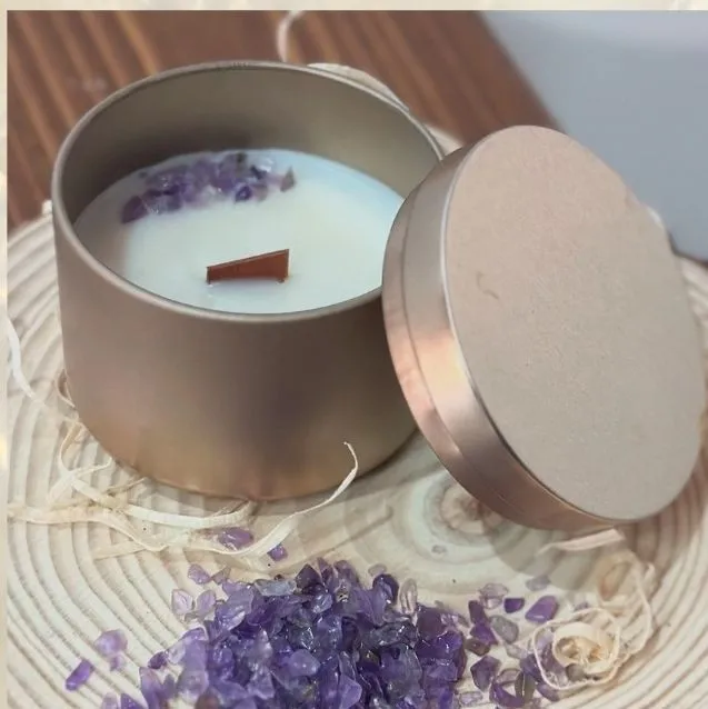 Candela in latta dorata con scaglie di ametista viola sulla cera, accanto al coperchio e a cristalli sparsi