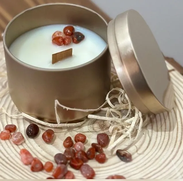 Candela in latta dorata con pietre di onice sulla superficie di cera, accanto al coperchio e a pietre sparse